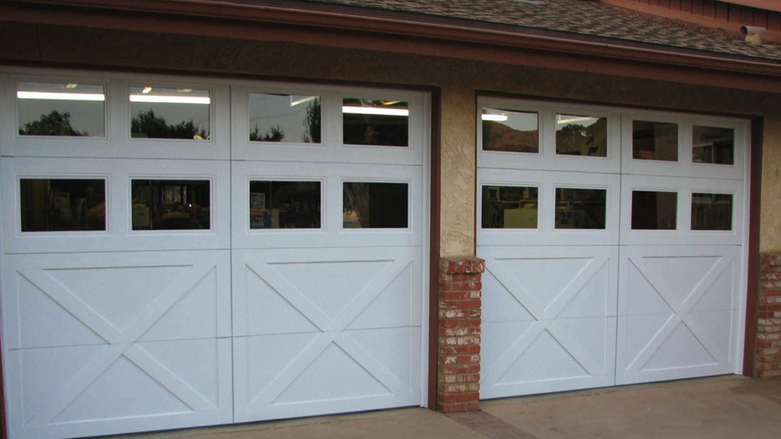 Modern farmhouse with white carriage-style garage doors, crossbuck design, dual windows, and brick column accent.