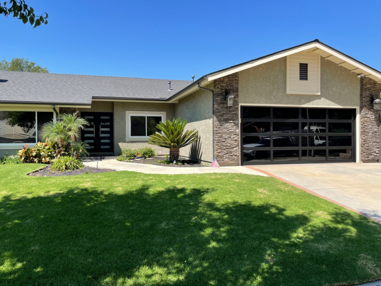 A house with a green lawn, a large black garage door, and a modern entryway with black double doors.